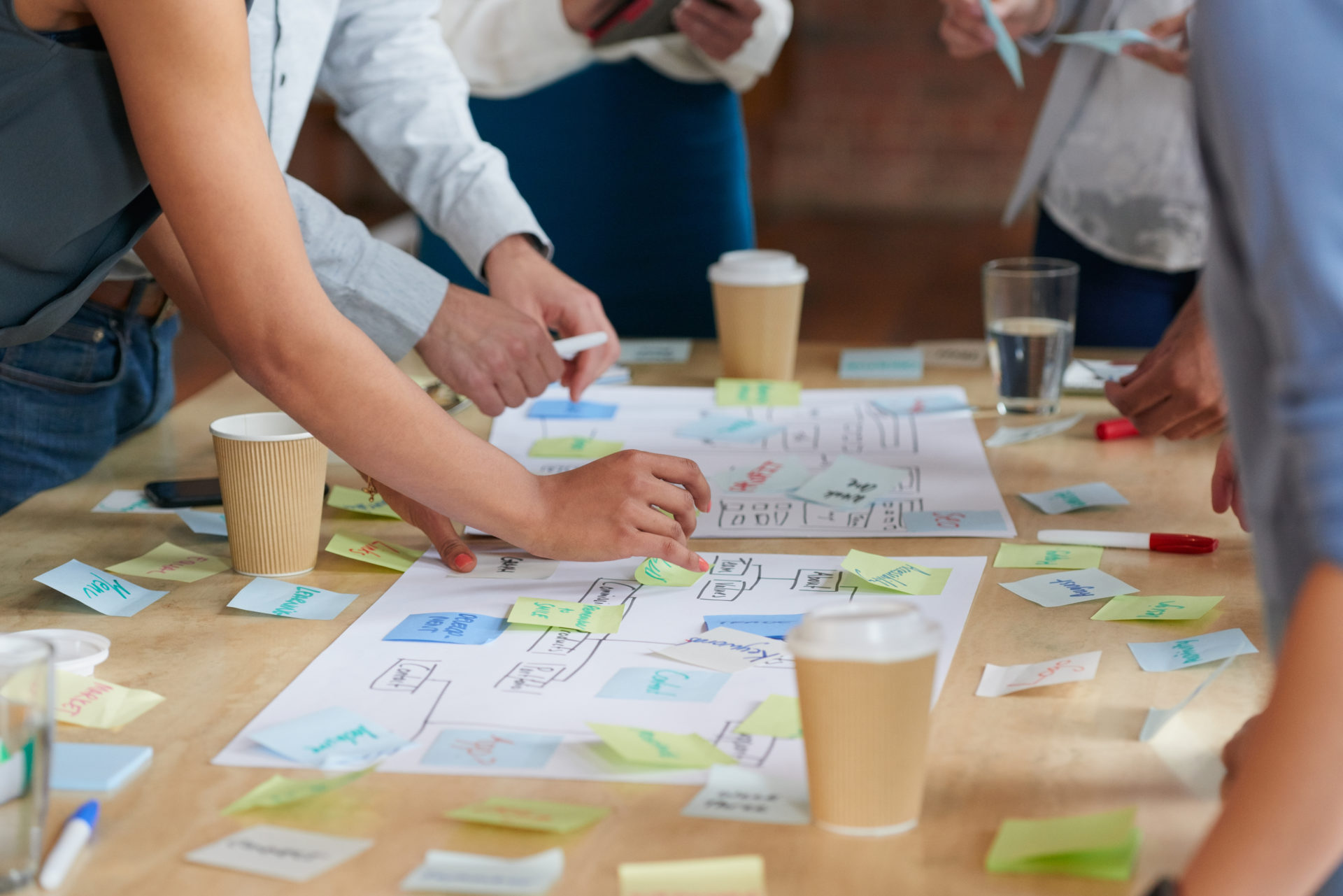 wooden table with employees working on brainstorming with sticky notes large sheets of paper and coffee